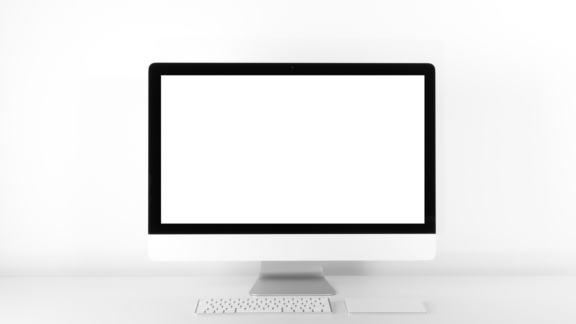 Stationär dator som står framför vit vägg med tangentbord framför som är placerad på vit bord. På skärmen visas en vit bakgrund