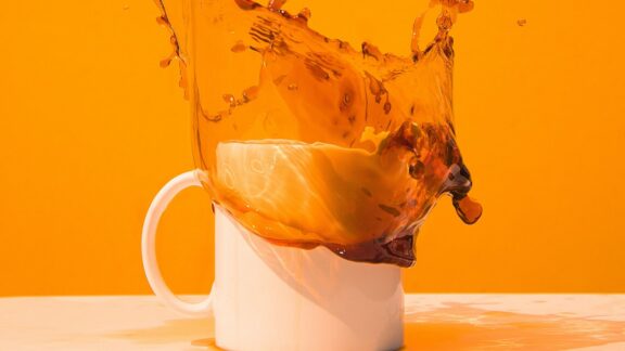 orange bakgrund med vit kaffekopp med kaffe som skvätter