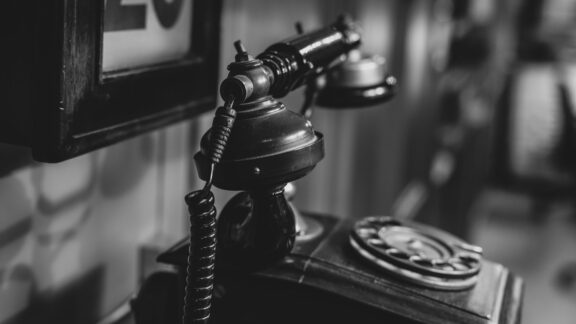 äldre telefon ståendes på bord med tavla i bakgrunden i svart och vit färg