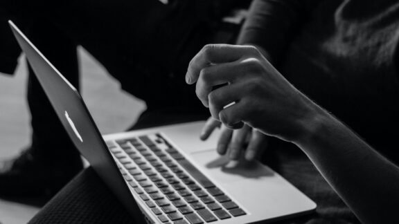 Kvinna med dator i knä med händer på tangentbord svart och vit färg